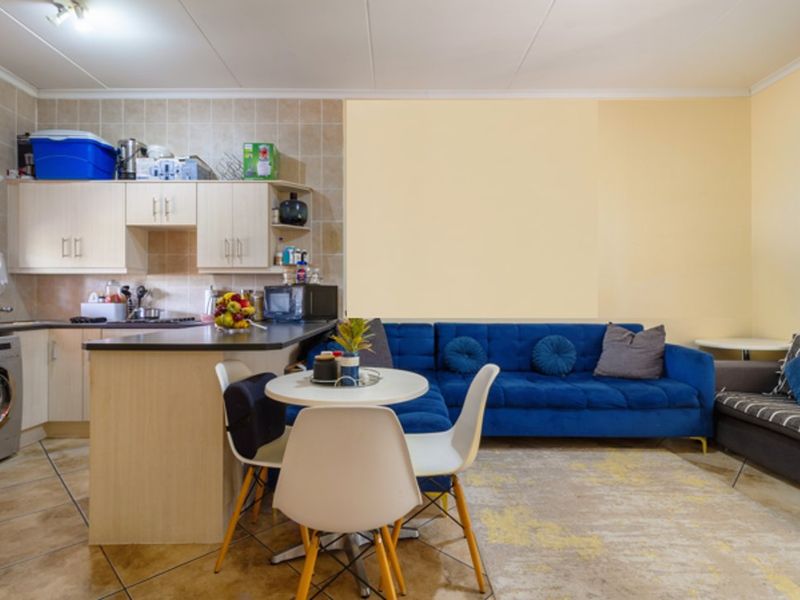 Open-plan living area featuring a functional kitchen with built-in cabinetry, tiled backsplash, and integrated laundry facilities, seamlessly flowing into the lounge space.