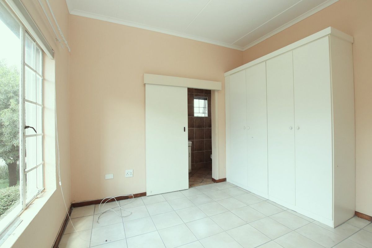 A vacant bedroom featuring built-in cupboards, tiled flooring, and a sliding door leading to an en-suite bathroom.