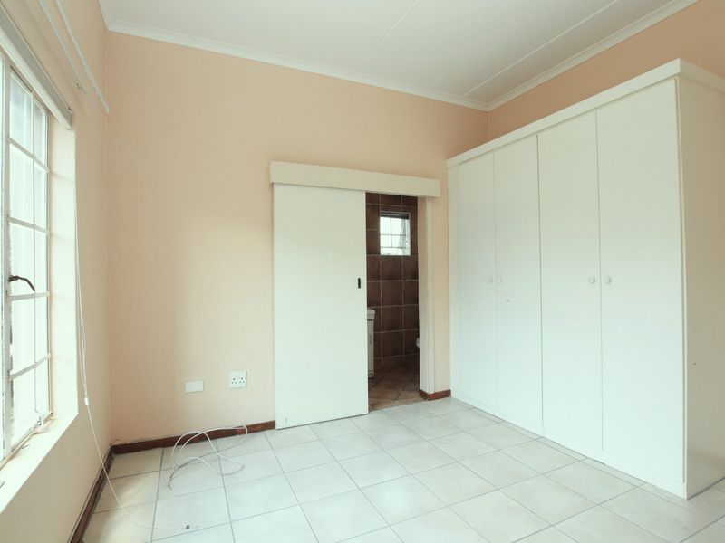 A vacant bedroom featuring built-in cupboards, tiled flooring, and a sliding door leading to an en-suite bathroom.