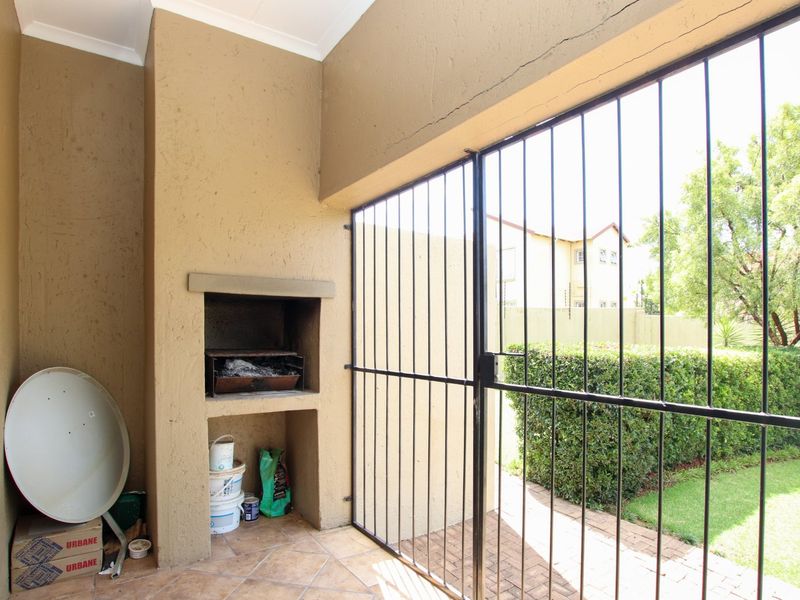 Covered patio area featuring a built-in braai, tiled flooring, and a secure metal gate leading to the garden.