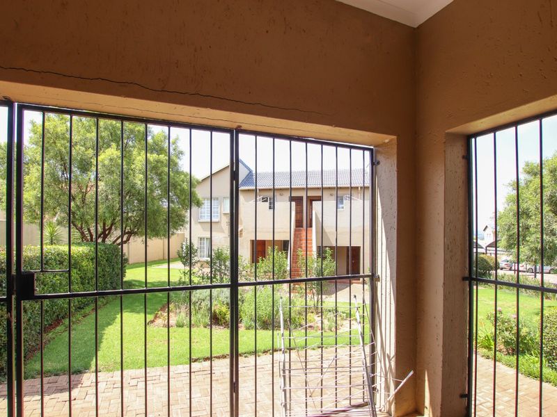 A covered patio area featuring paved flooring and security gates, overlooking a communal garden space.