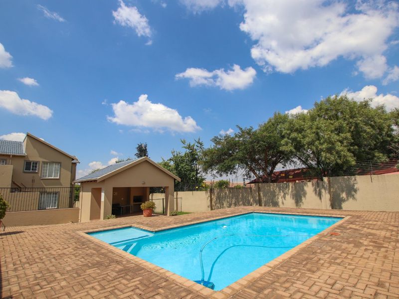 Outdoor pool area featuring a paved deck, a covered entertainment structure, and secure perimeter walling with electric fencing.