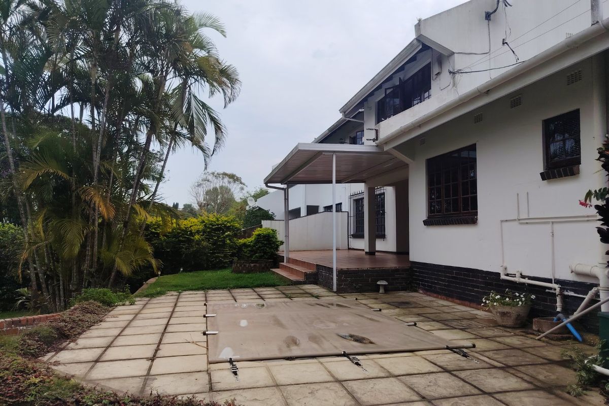 Rear exterior view featuring a covered patio area, paved pool deck with cover, and established garden surroundings.