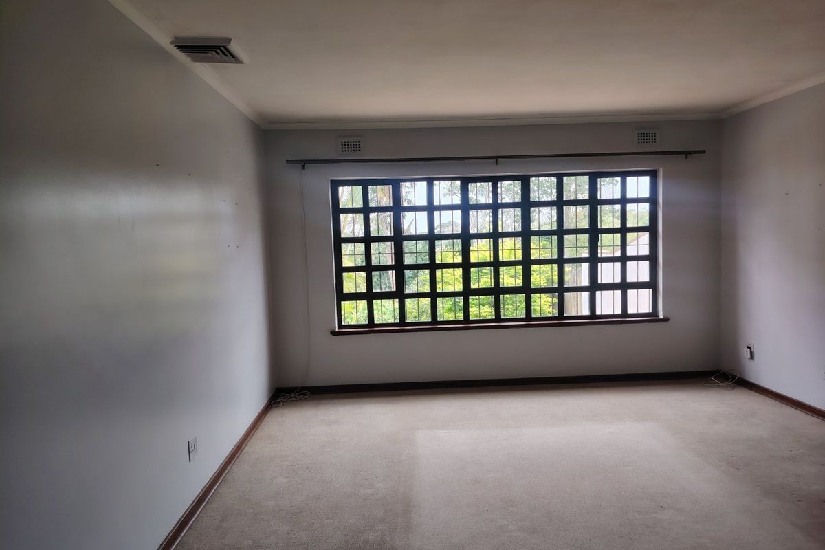 An empty living room featuring a large grid-pattern window, neutral wall finishes, and carpet flooring, offering a blank canvas for interior design.