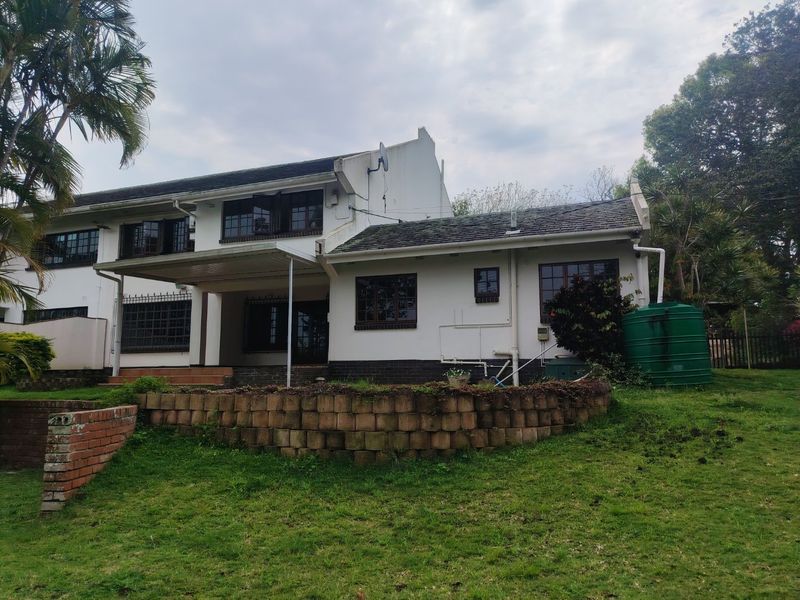 Rear view of the house featuring a covered patio, a brick retaining wall, and a water tank set within a garden area.