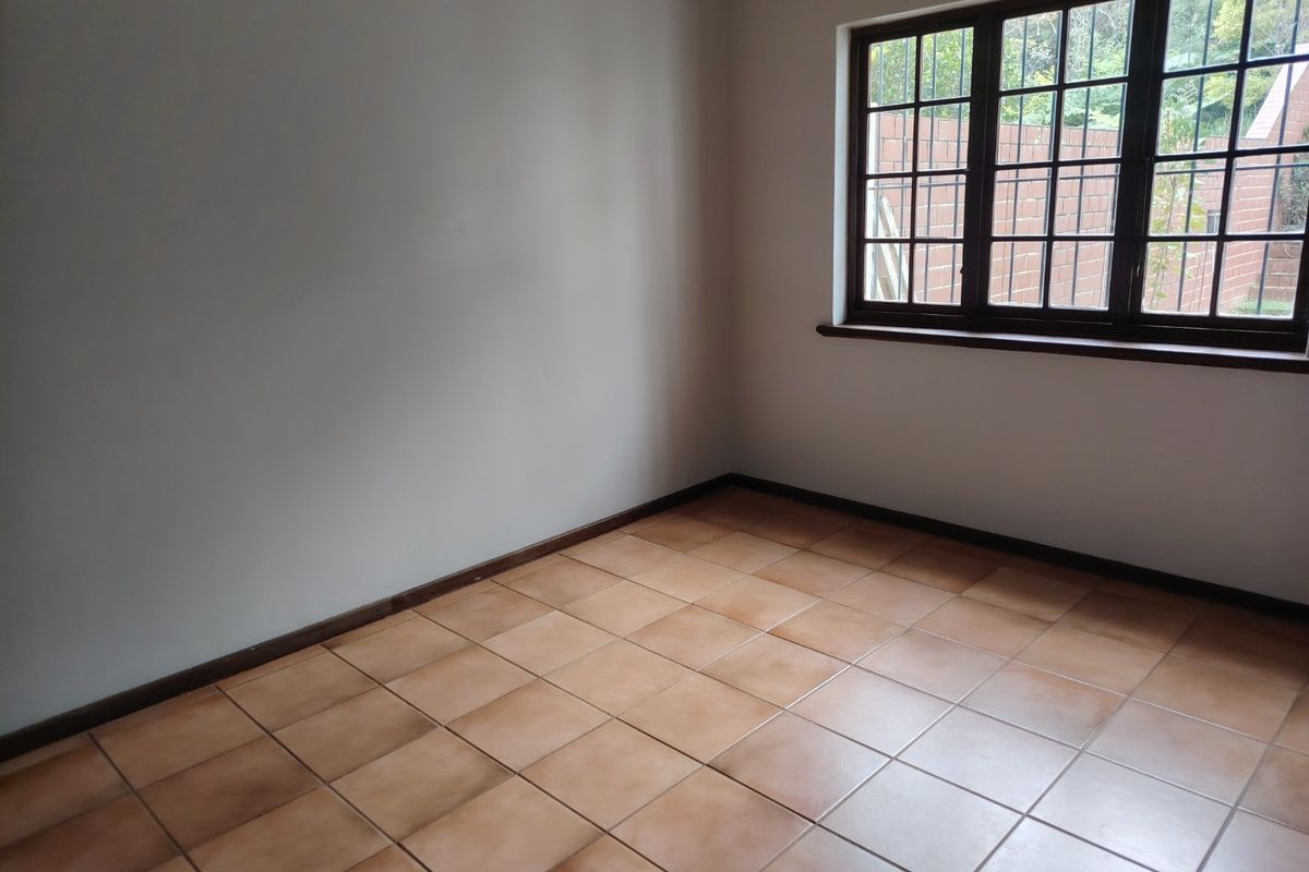A bright, empty bedroom featuring neutral walls, tiled flooring, and a window with security bars, offering a clean canvas for personalization.