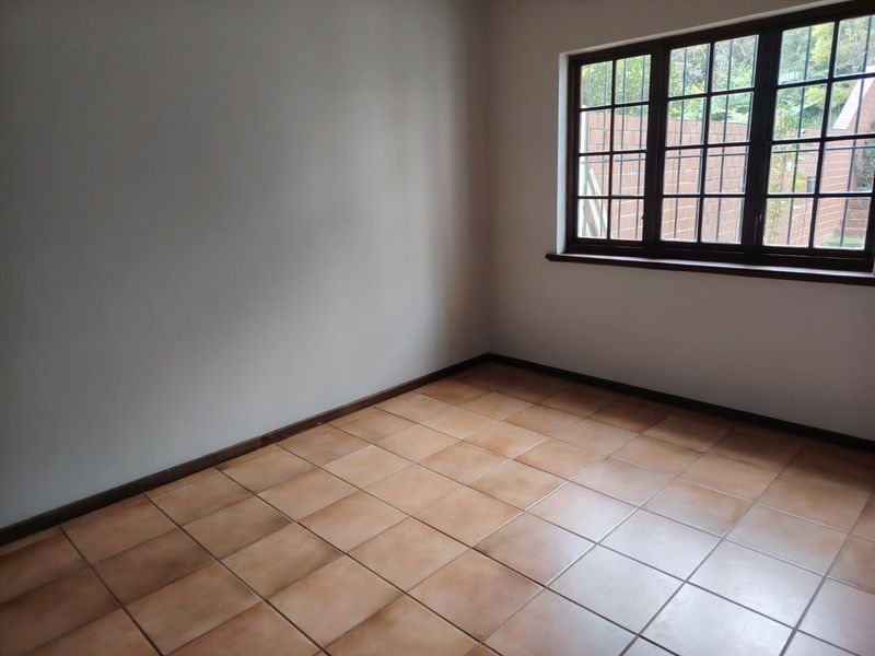 A bright, empty bedroom featuring neutral walls, tiled flooring, and a window with security bars, offering a clean canvas for personalization.