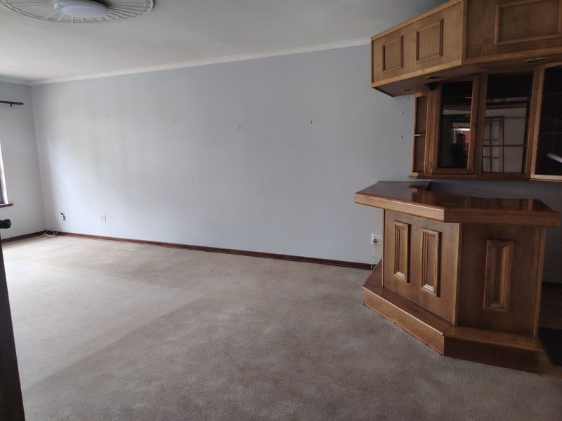 An empty living area featuring a built-in wooden bar unit, carpeted flooring, and a decorative ceiling rose.