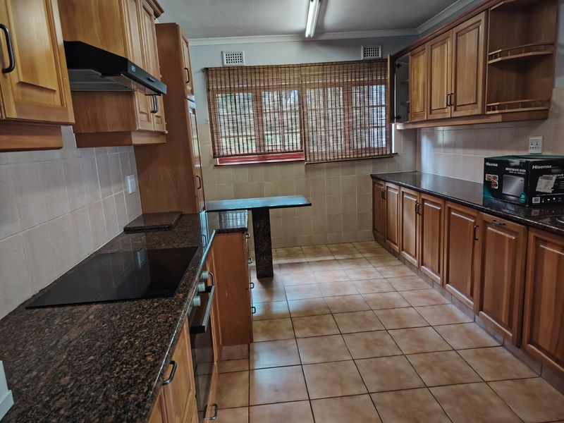 A functional kitchen featuring wooden cabinetry, granite countertops, built-in oven and hob, and tiled flooring throughout.
