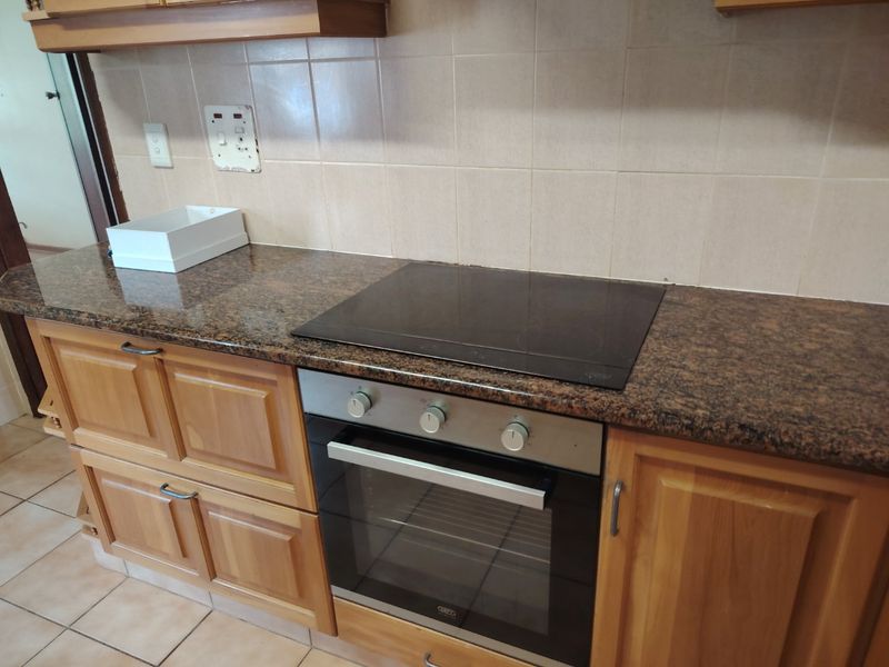 A functional kitchen area featuring wooden cabinetry, granite countertops, a built-in oven, and an electric hob with a tiled backsplash.