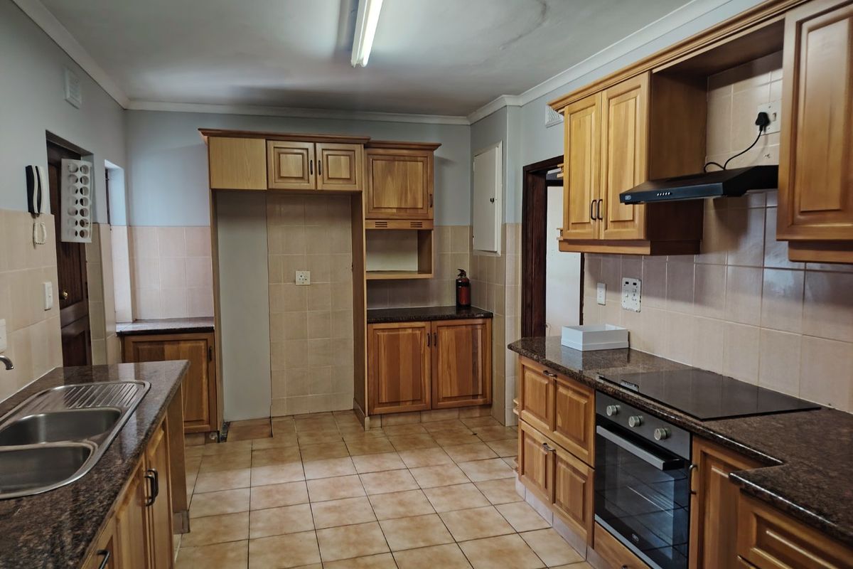 A functional kitchen featuring wooden cabinetry, granite countertops, a built-in oven with hob, and tiled finishes throughout.