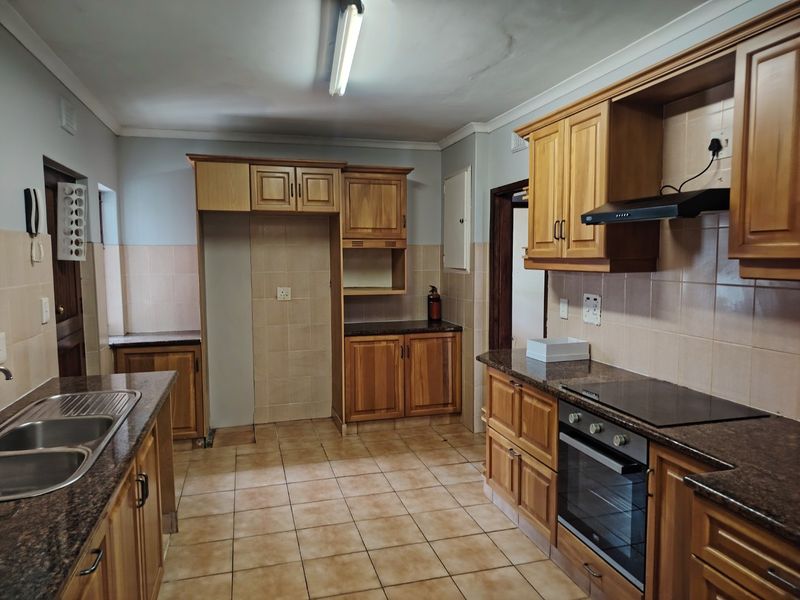 A functional kitchen featuring wooden cabinetry, granite countertops, a built-in oven with hob, and tiled finishes throughout.