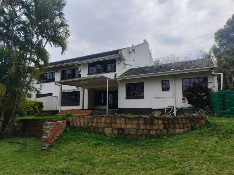 Rear view of a two-story house featuring a covered patio, retaining wall, and rainwater tank, showing signs of exterior wear and maintenance needs.