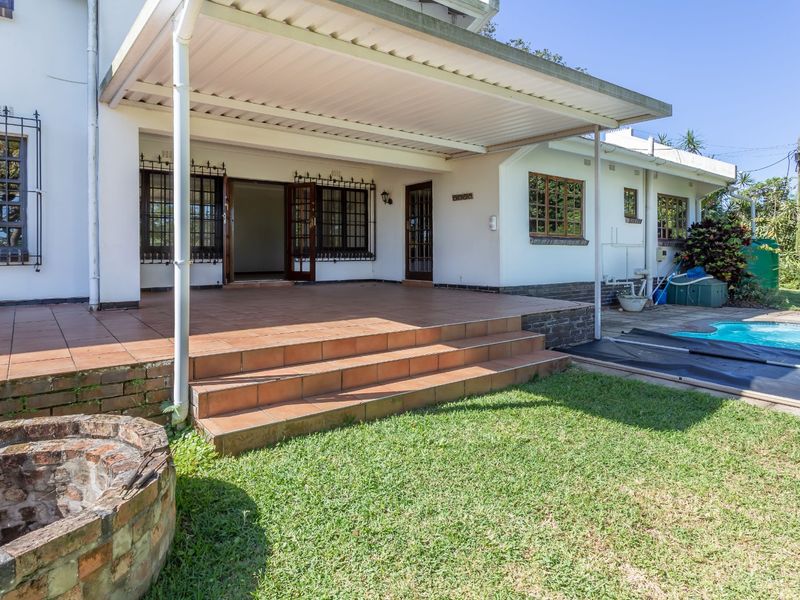 A spacious covered patio featuring tiled flooring and security bars, overlooking a private swimming pool and garden area.