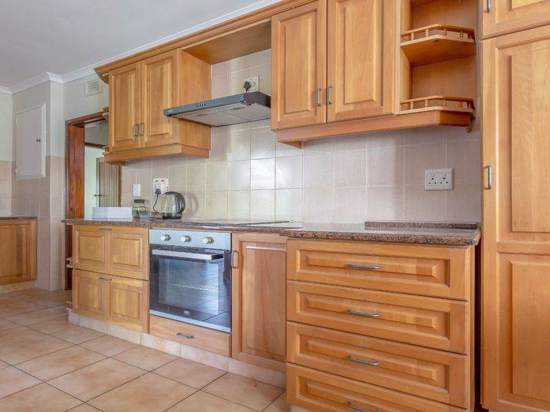A functional kitchen featuring wooden cabinetry, granite countertops, a built-in oven, and an extractor fan with tiled flooring and backsplash.
