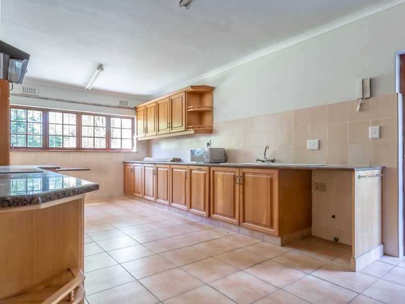 Spacious kitchen featuring wooden cabinetry, granite countertops, tiled backsplash, and tiled flooring, offering a functional layout with direct access to an exterior security gate.