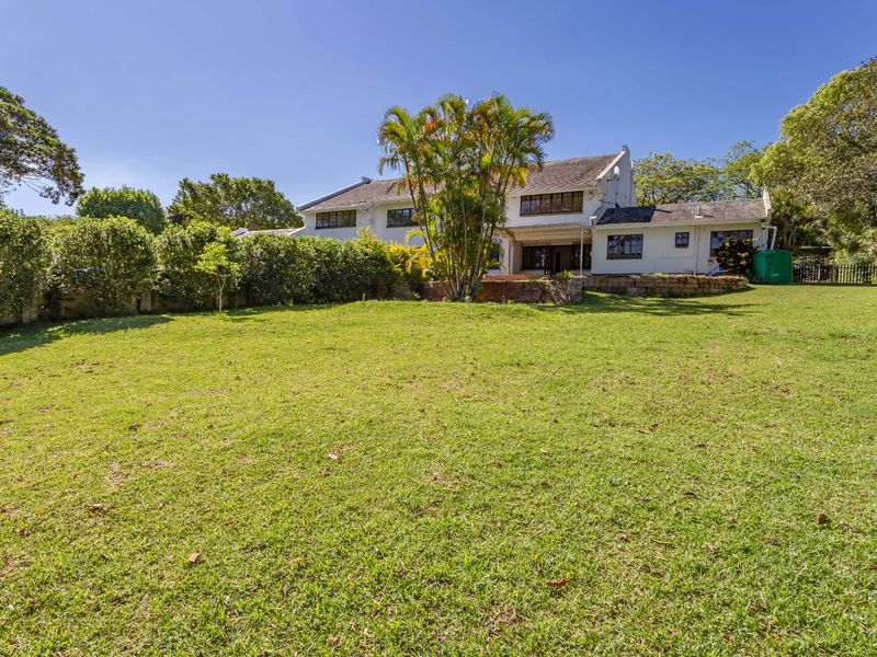 Spacious rear garden featuring a large lawn, established hedging, and a brick retaining wall leading to the main house structure.