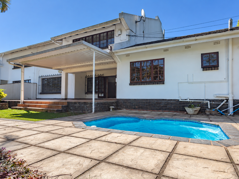Rear exterior view of the house featuring a swimming pool, paved patio area, and a covered patio structure.