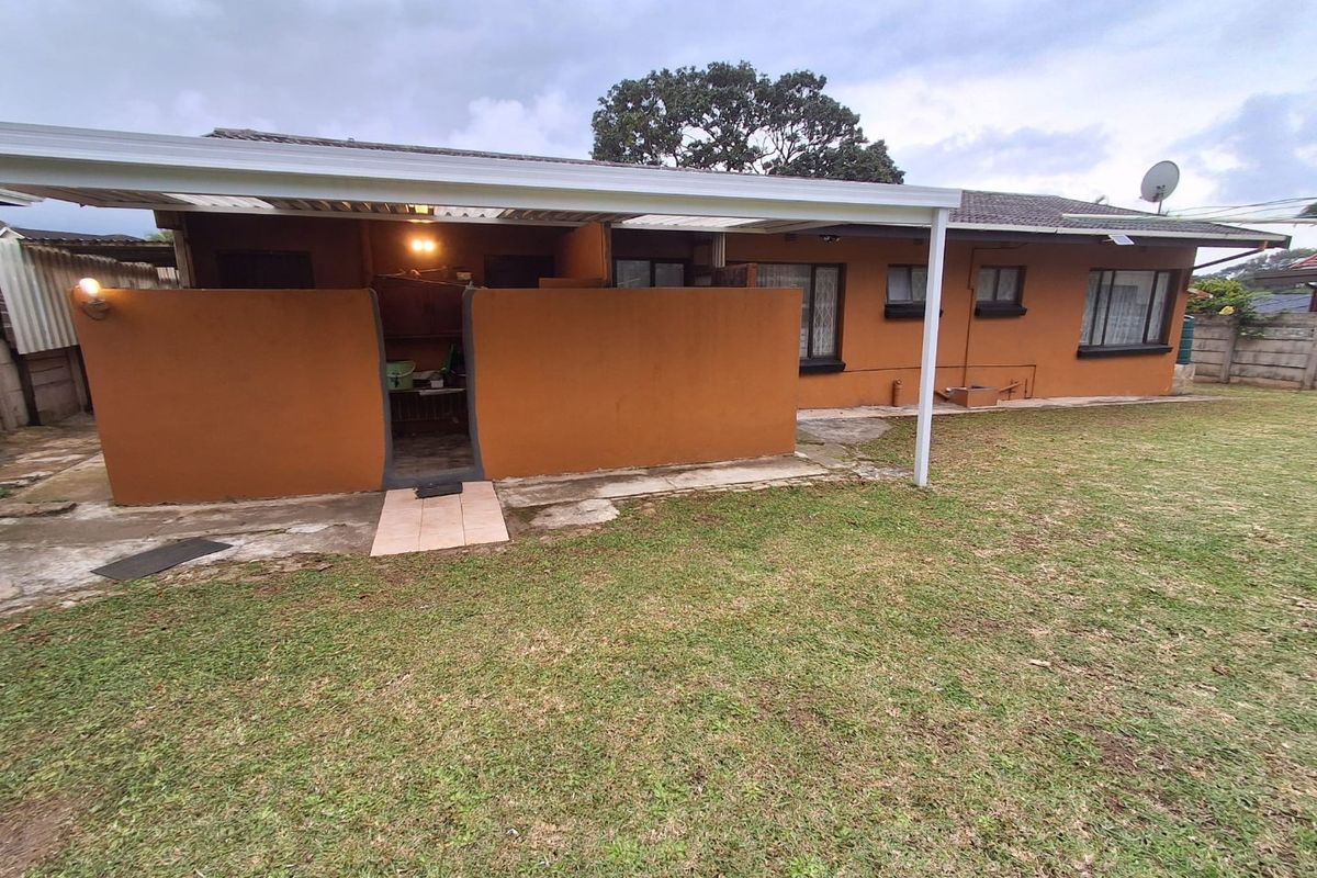 Rear view of the property featuring a covered patio area, paved walkway, and a spacious lawn with established garden surroundings.