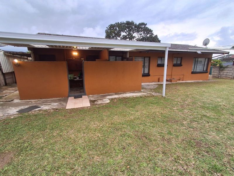 Rear view of the property featuring a covered patio area, paved walkway, and a spacious lawn with established garden surroundings.