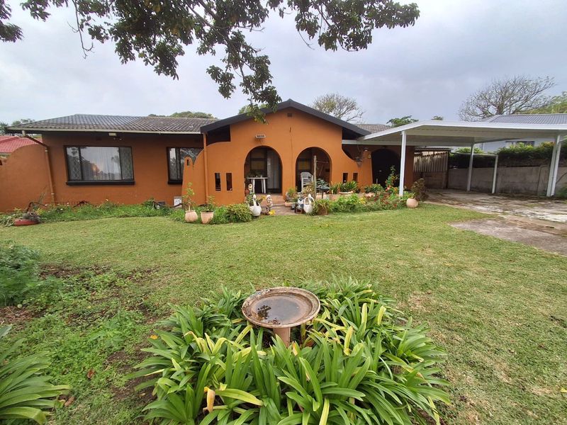 Front view of a single-story house featuring an arched entrance, a tiled roof, and an attached carport with a front garden.
