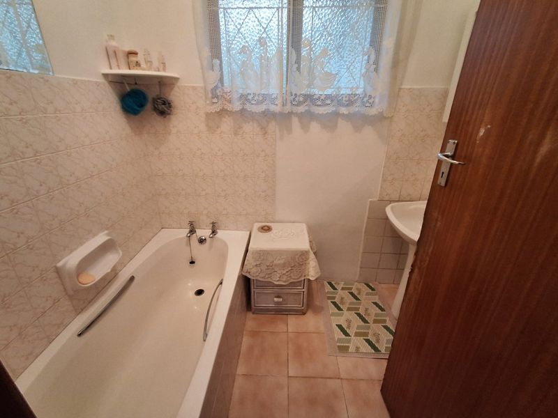 A compact bathroom featuring a standard bathtub, pedestal basin, and tiled finishes, offering a functional space with potential for modern updates.