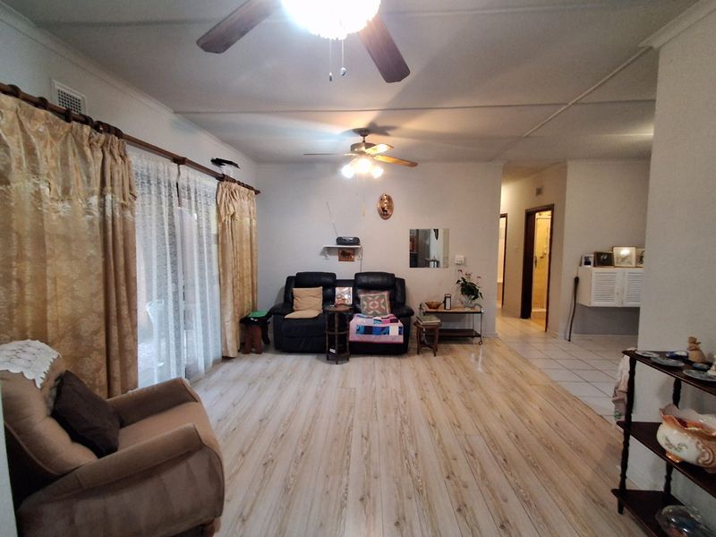 A spacious living room featuring light-toned laminate flooring, dual ceiling fans, and a large sliding glass door providing access to the exterior.