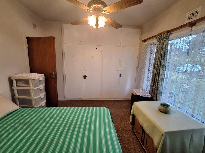 A bedroom featuring built-in wardrobes, a ceiling fan, and carpet flooring, offering a functional space with potential for modern updates.