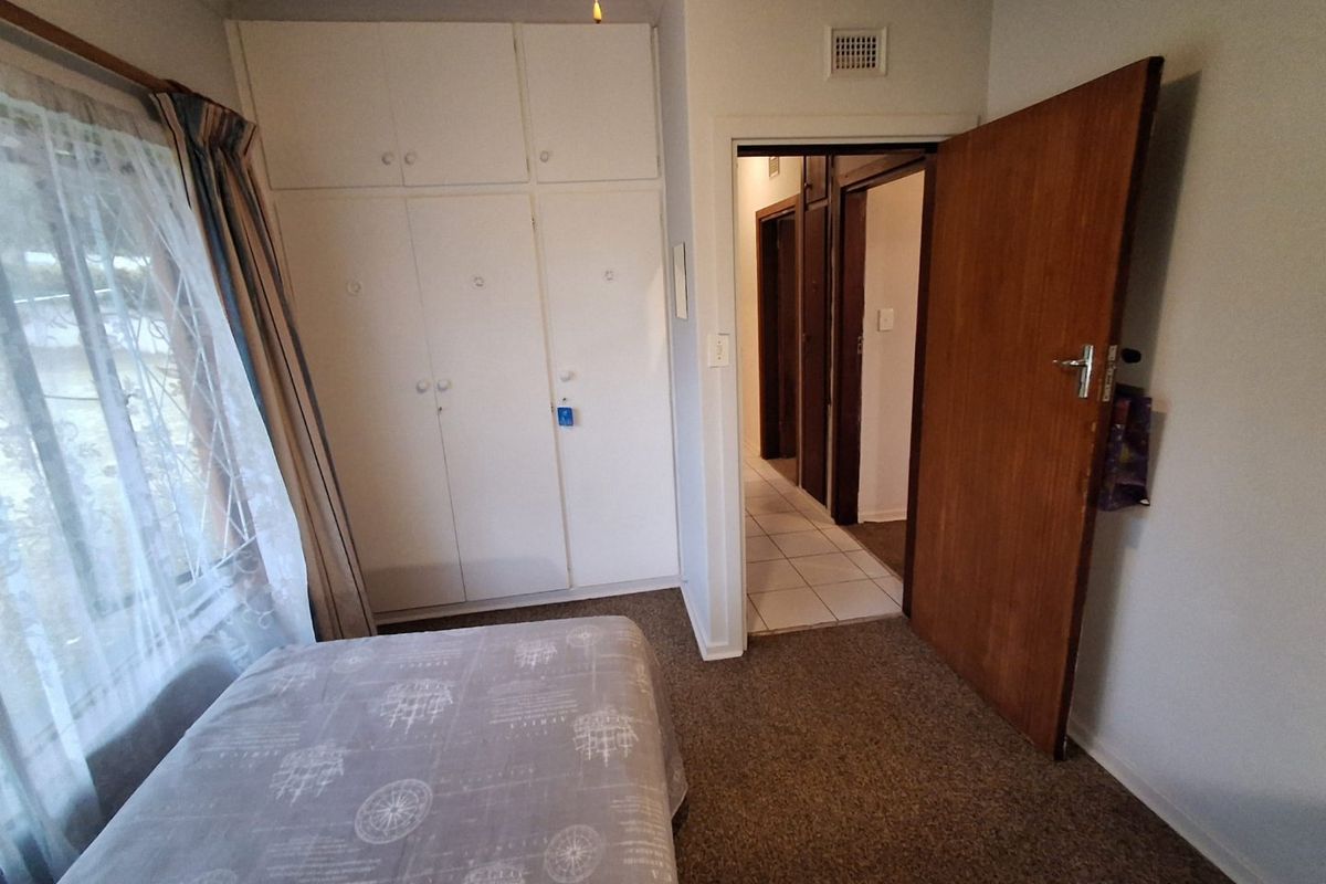 A functional bedroom featuring built-in cupboards, carpeted flooring, and direct access to the hallway.