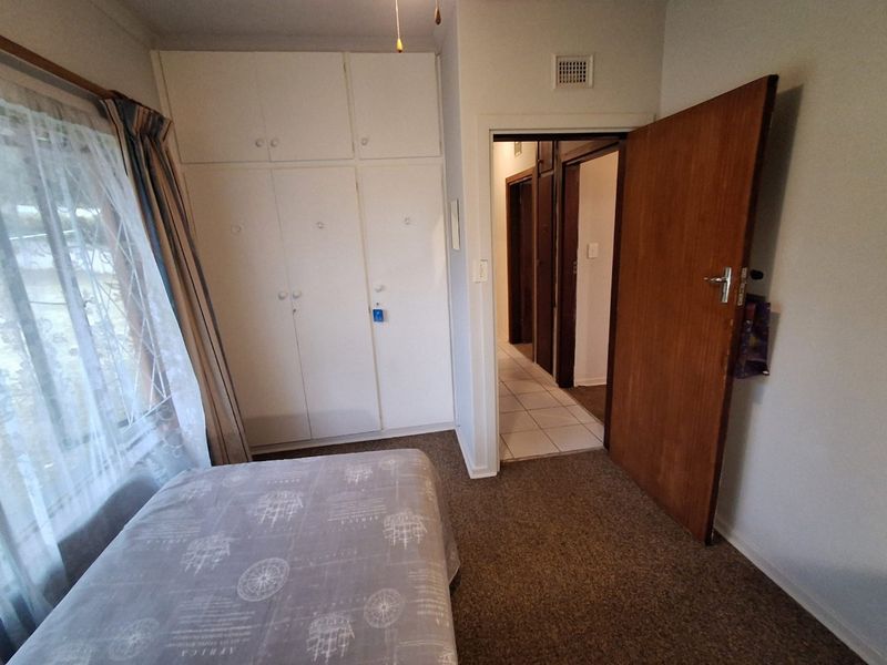 A functional bedroom featuring built-in cupboards, carpeted flooring, and direct access to the hallway.