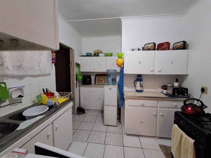 Functional kitchen featuring white built-in cabinetry, tiled splashbacks, and tiled flooring, offering a practical layout with ample storage space.
