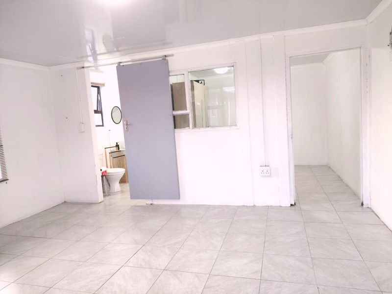 An empty living area featuring tiled flooring, a sliding door, and an internal window, providing a blank canvas for interior design.