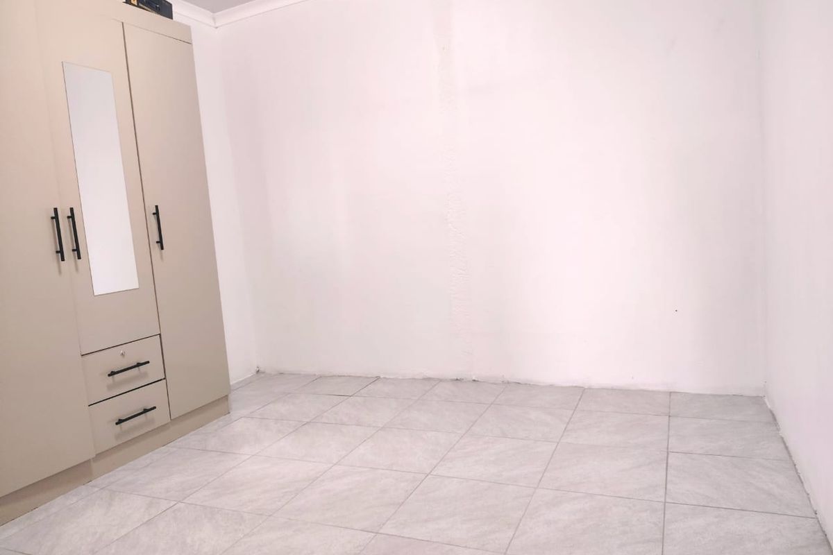 A clean, empty bedroom featuring neutral tiled flooring and a built-in wardrobe with a mirrored panel.