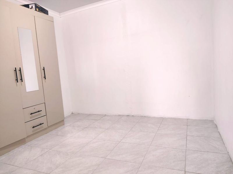 A clean, empty bedroom featuring neutral tiled flooring and a built-in wardrobe with a mirrored panel.