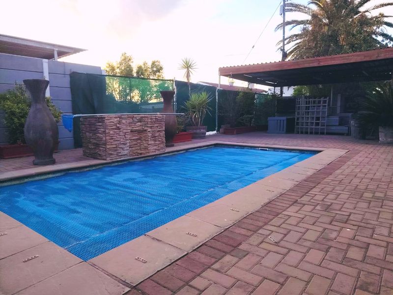 Outdoor pool area featuring a paved patio, a timber pergola, and a stone-clad water feature, providing a functional space for relaxation.