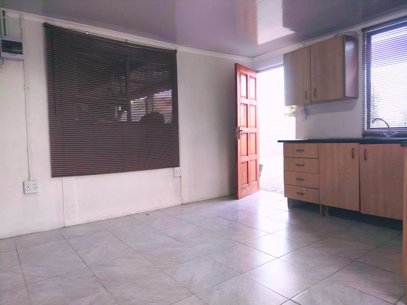 Open plan living area featuring tiled flooring, built-in kitchen cabinetry with laminate countertops, and direct access to the exterior.