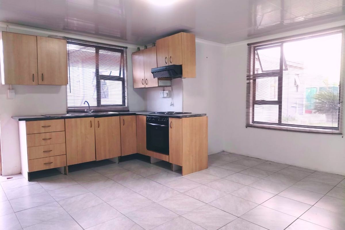 A functional, empty kitchen featuring light wood-tone cabinetry, built-in oven, extractor fan, and tiled flooring with ample natural light from two windows.