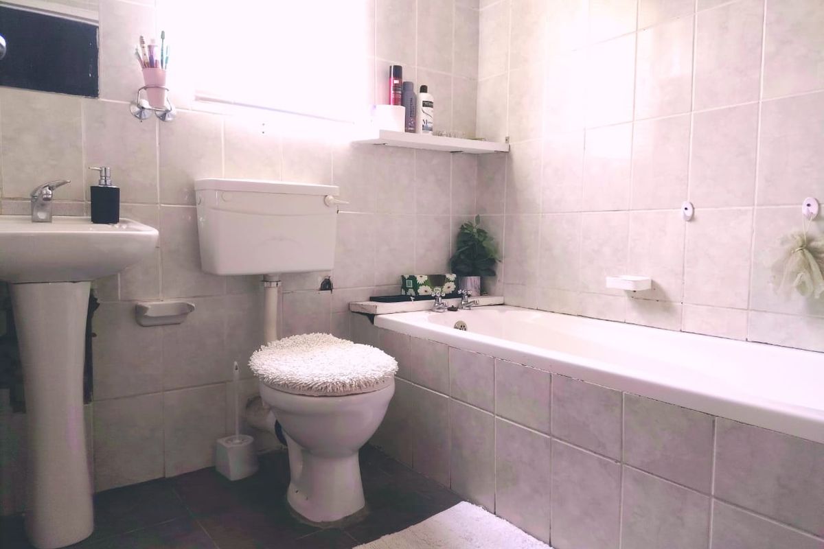 A functional bathroom featuring a pedestal basin, standard toilet, and a tiled bathtub with wall-to-wall tiling.