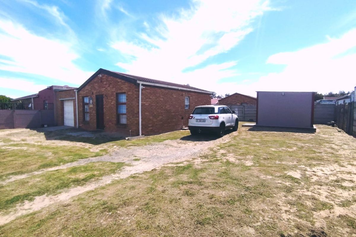 Front view of a single-story brick house featuring a tiled roof, attached garage, and a large unpaved yard area.