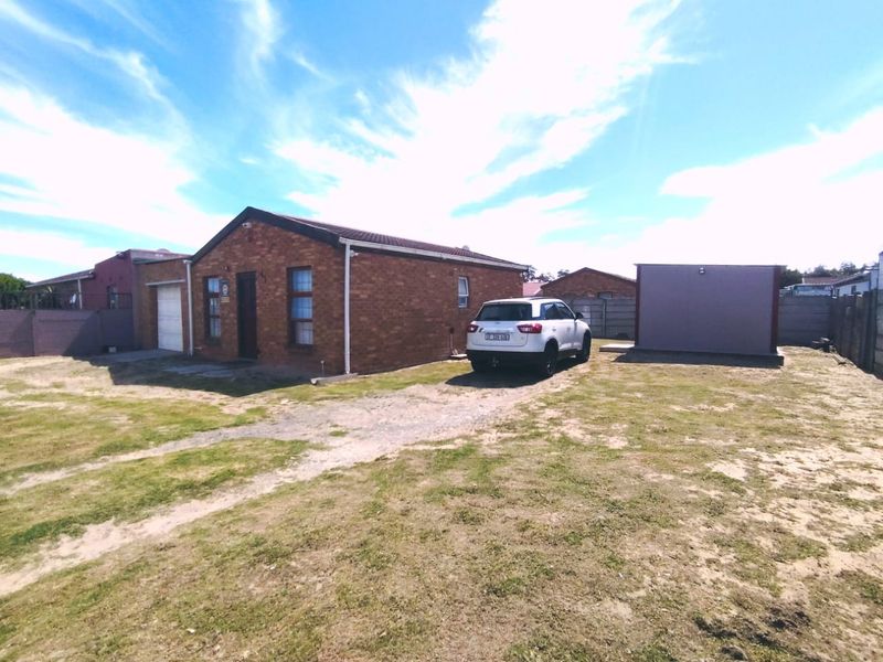 Front view of a single-story brick house featuring a tiled roof, attached garage, and a large unpaved yard area.