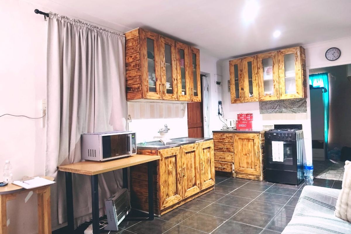 A functional kitchen featuring wooden cabinetry, a stainless steel sink, and a freestanding stove, complemented by dark tiled flooring.