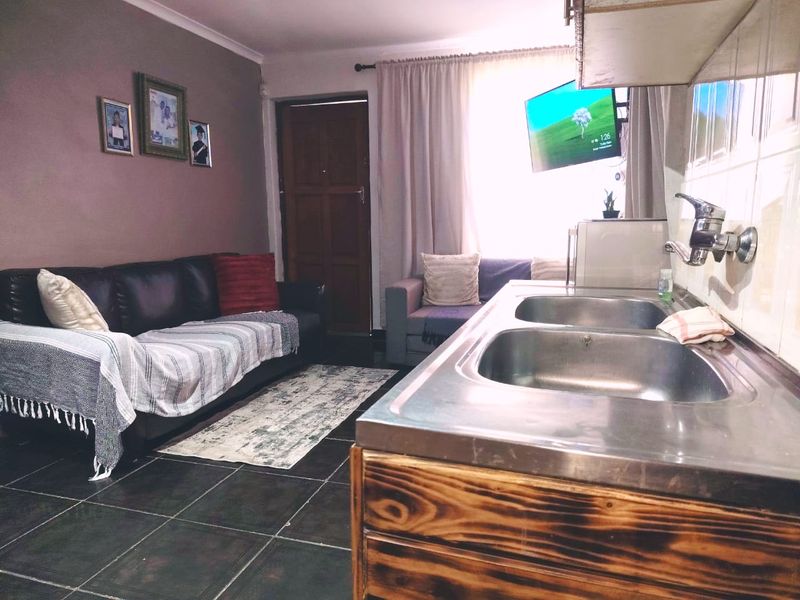 Open-plan living area featuring a compact kitchenette with a double stainless steel sink, tiled flooring, and direct access to the main entrance.
