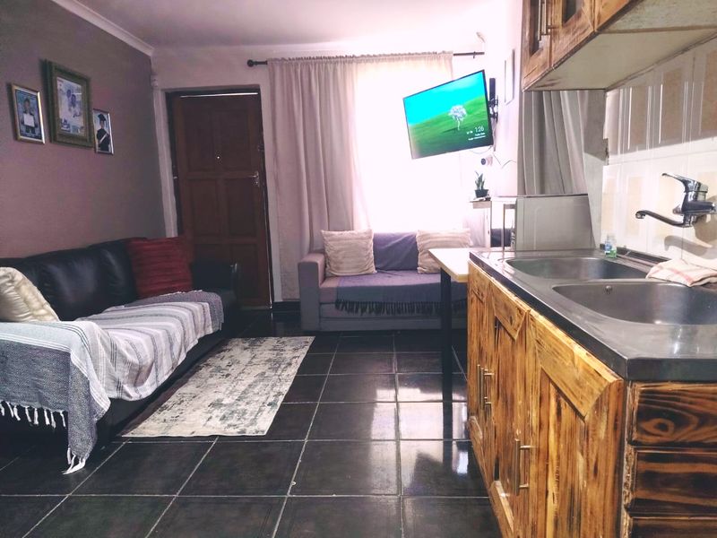 Open plan living area featuring tiled flooring and a compact kitchen with wooden cabinetry and a double sink.