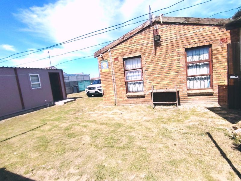Rear view of a face brick house featuring security bars on windows and a small garden area.
