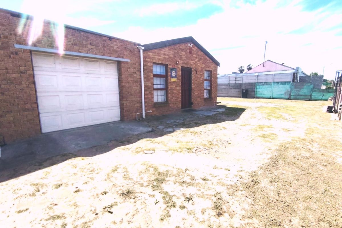 Rear view of a brick house featuring an attached garage, security gate, and a large backyard area with a precast boundary wall.