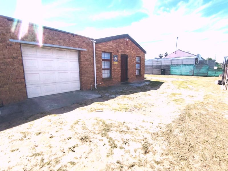 Rear view of a brick house featuring an attached garage, security gate, and a large backyard area with a precast boundary wall.