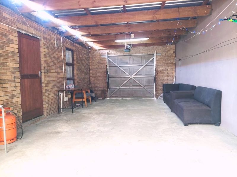 A functional garage space featuring exposed timber rafters, brick walls, and a concrete floor, equipped with a sectional garage door and motor.