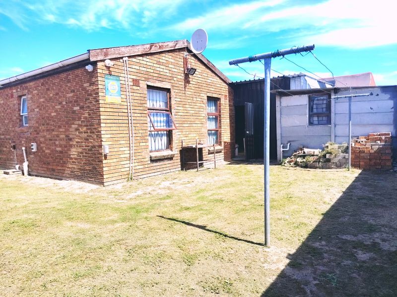 Rear view of a face brick house featuring a lawn area, security bars on windows, and a metal washing line.