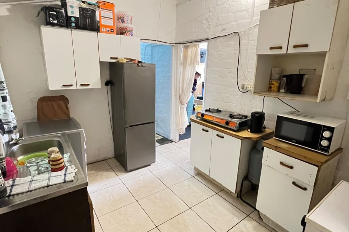 A functional kitchen featuring tiled flooring, built-in cabinetry, a gas hob, and exposed brick walls, offering potential for modernization and improved storage solutions.