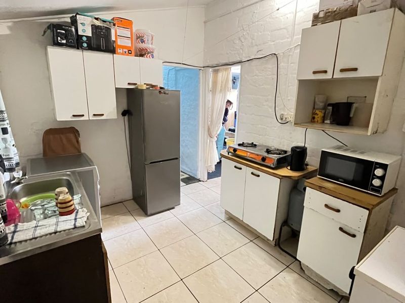 A functional kitchen featuring tiled flooring, built-in cabinetry, a gas hob, and exposed brick walls, offering potential for modernization and improved storage solutions.